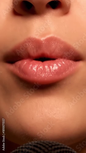 Closeup of a mouth with warm frontal lighting, glossy pink lips and teeth, slow opening and closing in a fixed shot. Static shot of speaking female mouth