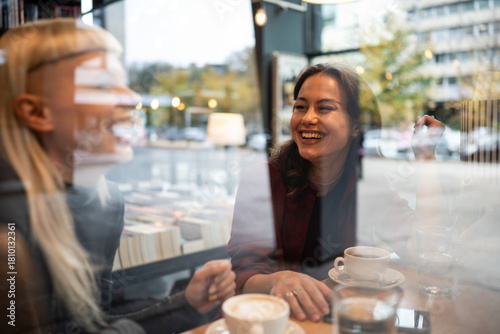 Fotografie Women friends laughing and enjoying coffee in cafe