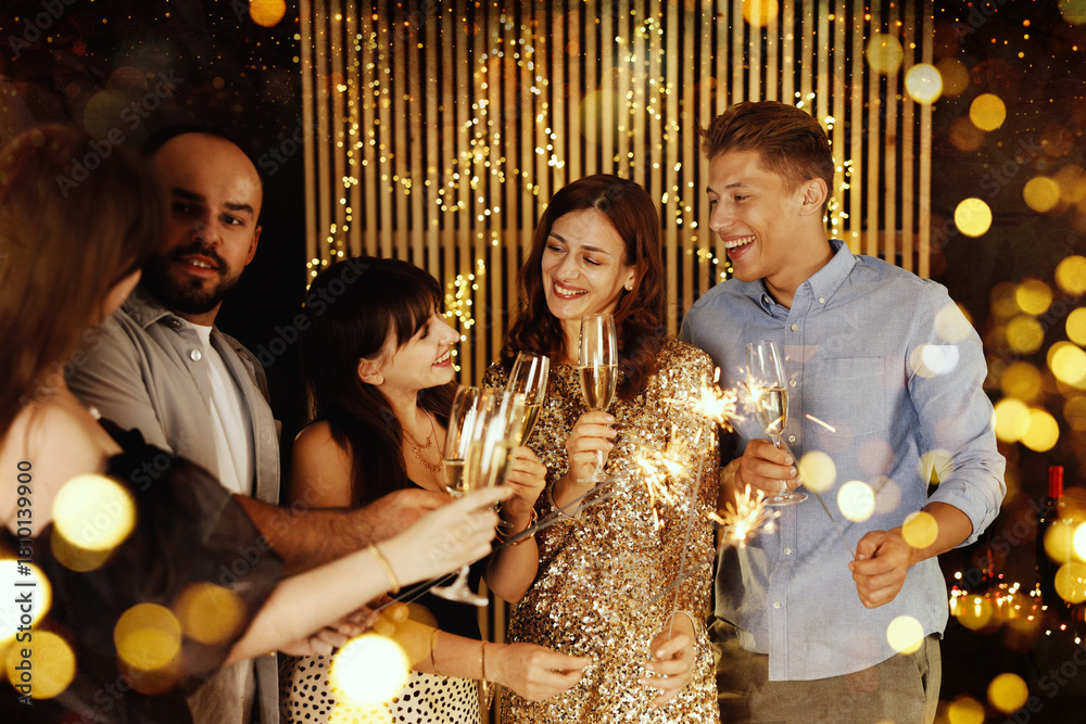 Fototapeta premium Happy New Year 2026 greeting card, bokeh lights. Friends celebrating with sparklers and wine glasses indoors
