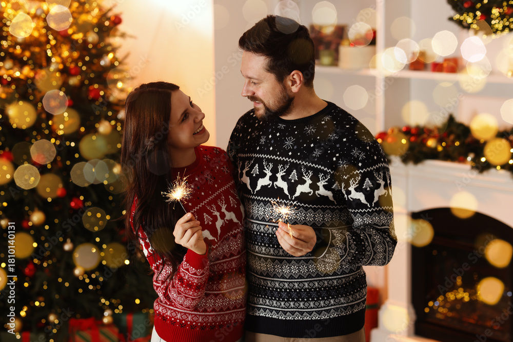 Fototapeta premium Happy New Year 2026 greeting card, bokeh lights. Lovely couple with sparklers together near Christmas tree in room