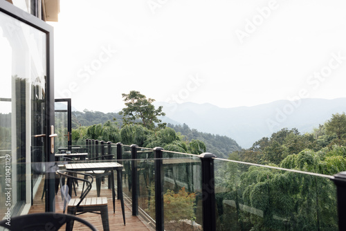Glass balcony with wooden furniture overlooking lush green forest and mountains