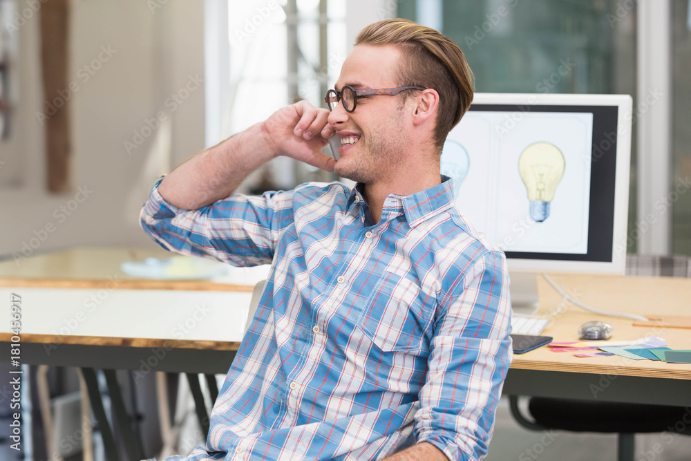 Fototapeta premium Man phoning, smiling, sitting at wood desk in open office with monitor lightbulbs and swatches