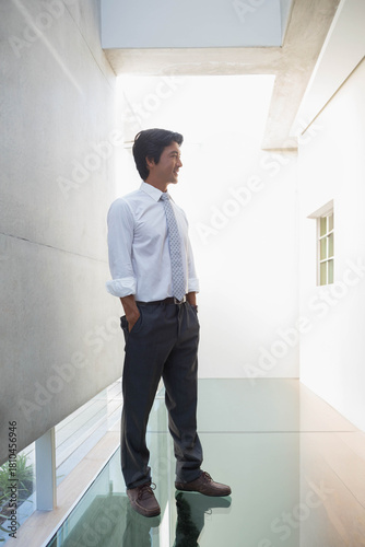 Canvas-taulu Mid-adult Asian man standing in modern atrium on glass floor, wearing white shir