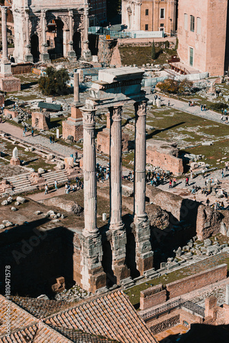 High angle view of three standing columns of the Temple of Castor and Pollux among the ruins of the Roman Forum, with scattered people.