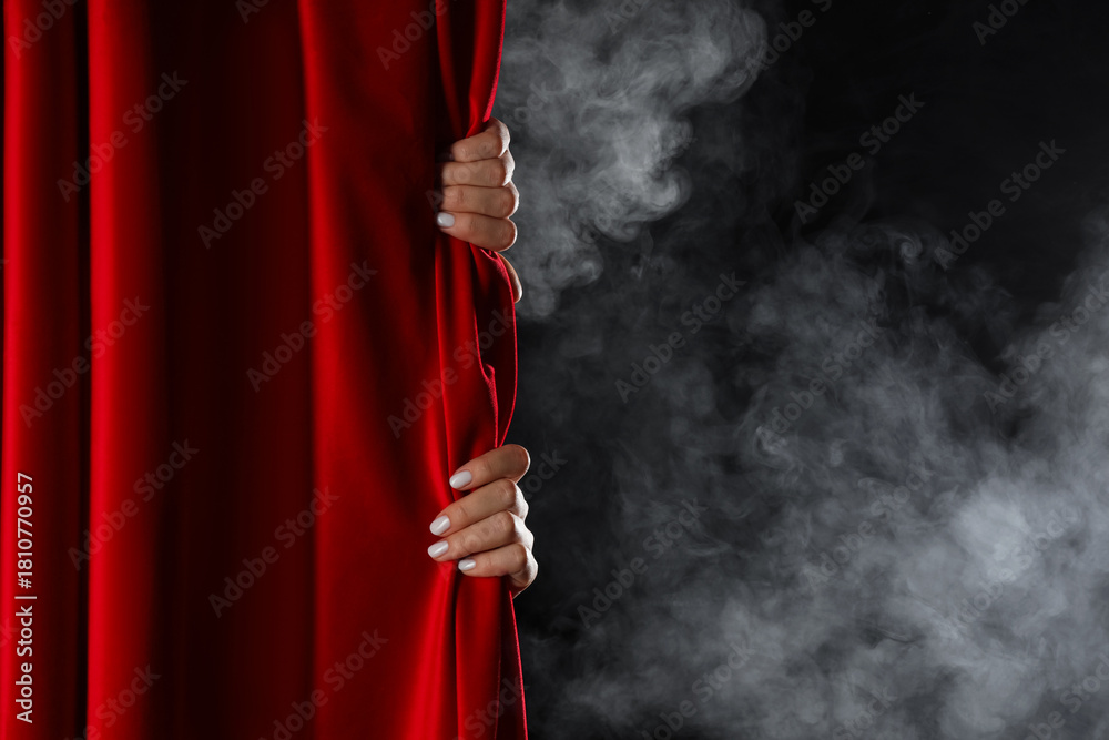 Fototapeta premium Female hands behind red curtain with smoke on dark background