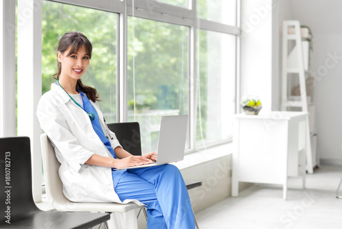 Female medical intern using laptop on chair in clinic