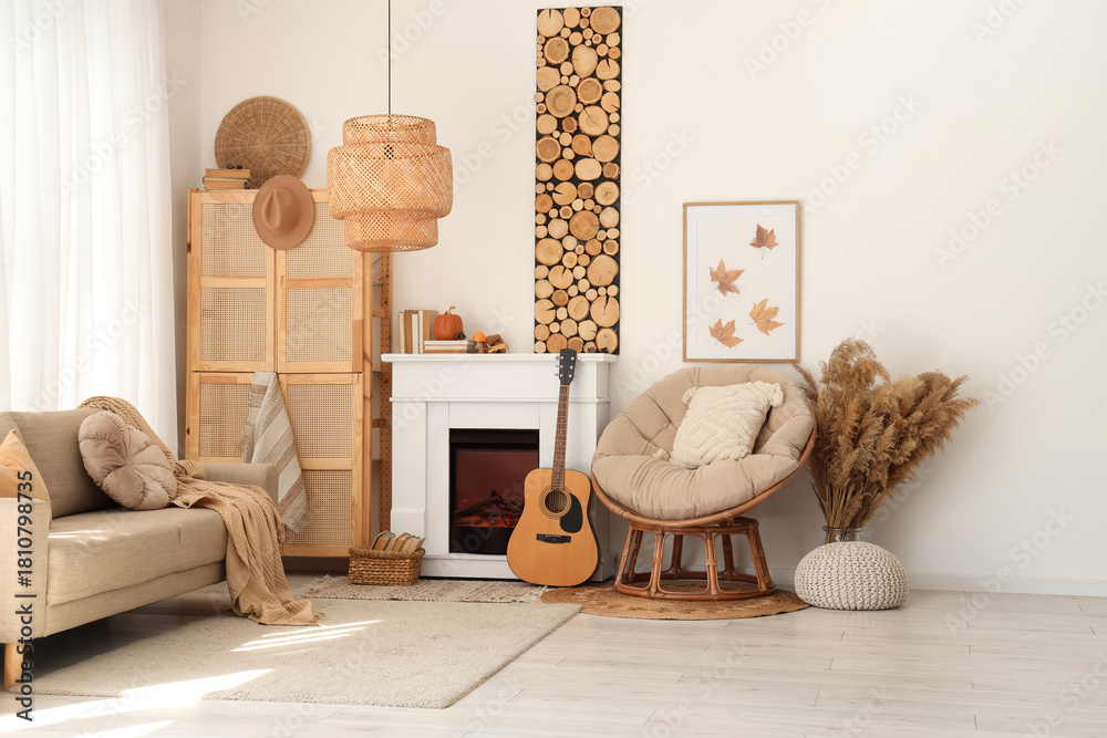 Naklejka premium Interior of living room with sofa, armchair, closet, guitar, fireplace and autumn home decor near white wall