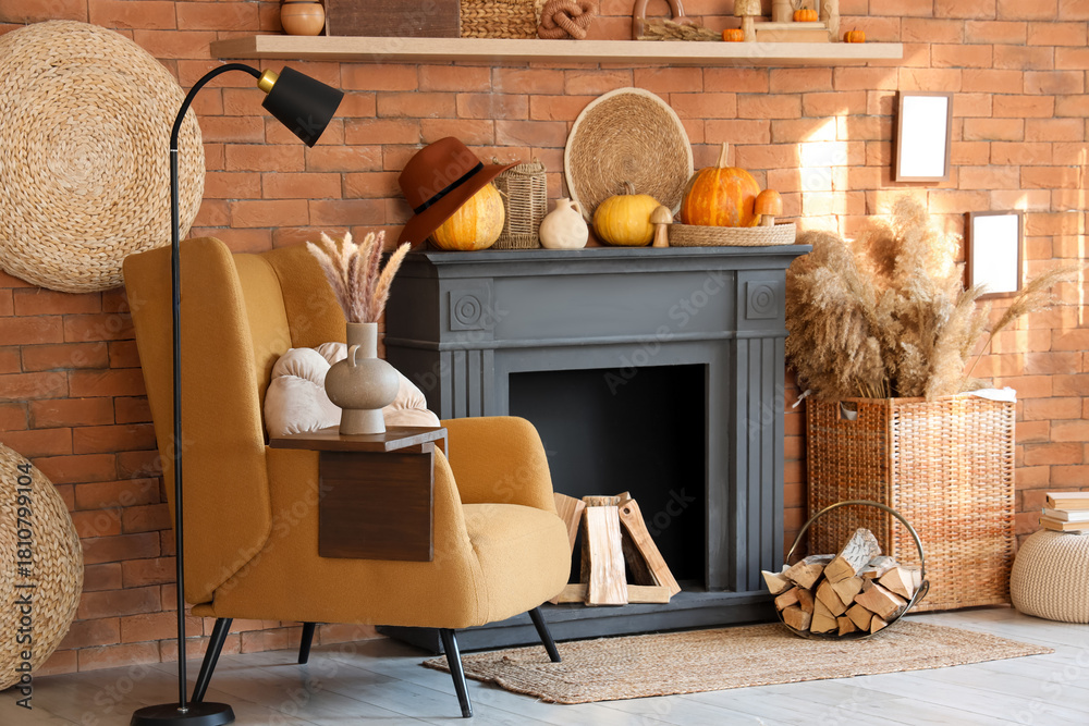 Fototapeta premium Interior of living room with armchair, lamp, pumpkins and autumn home decor on fireplace near brick wall