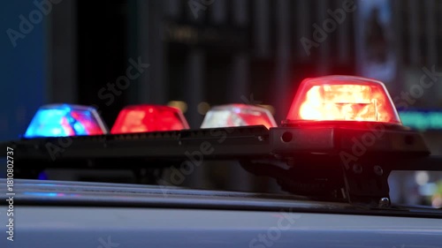 Closeup of a red police emergency light bar mounted on a vehicle roof against an urban city background, suitable for security, law enforcement, alert systems and public safety themed stock content