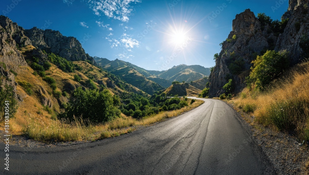 Naklejka premium Scenic winding road through a sunny mountain valley with clear blue sky