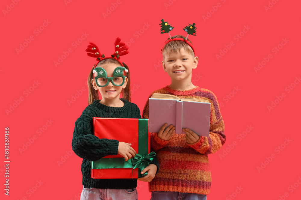 Fototapeta premium Cute little children with book and Christmas gift on red background