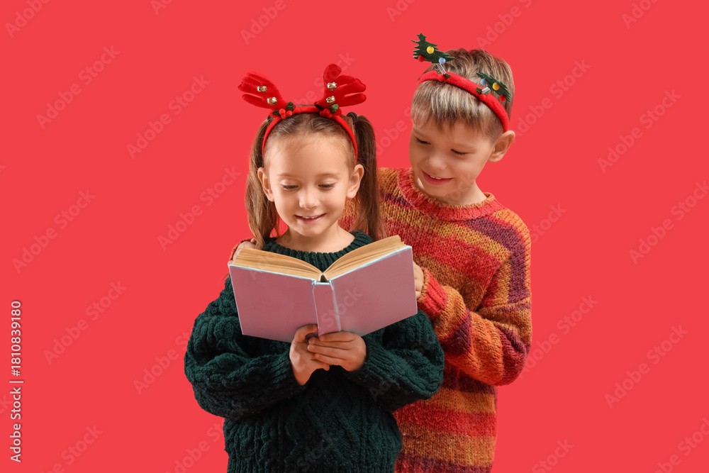 Naklejka premium Cute little children reading Christmas story on red background