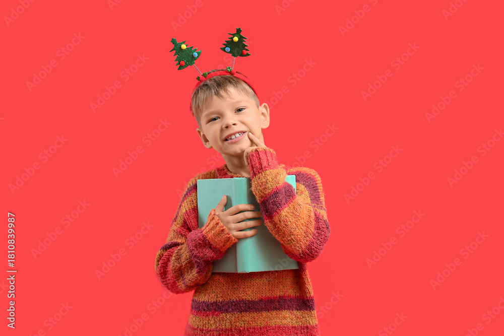 Naklejka premium Dreamy little boy with book on red background. Christmas celebration