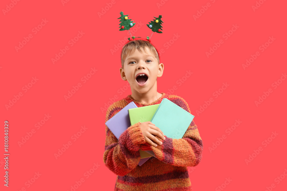 Naklejka premium Happy little boy with books on red background. Christmas celebration