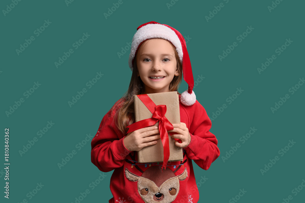 Naklejka premium Cute little girl in Santa hat with gift book on green background