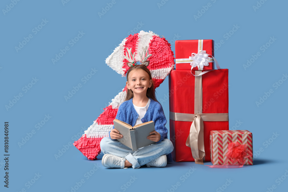 Naklejka premium Cute little girl with book and Christmas gifts sitting on blue background