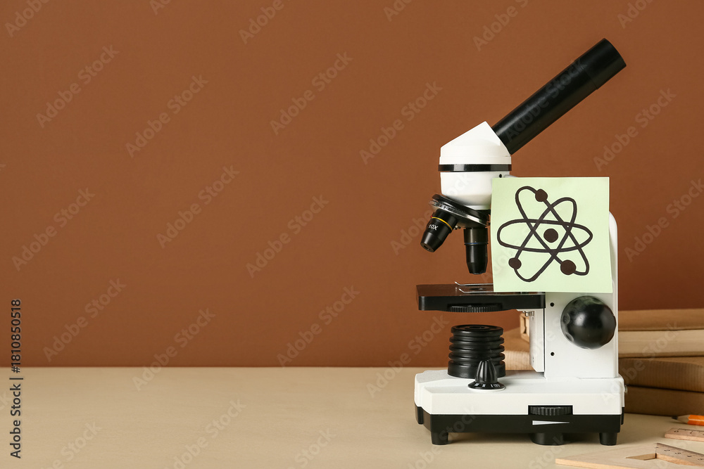 Fototapeta premium Microscope with drawn molecule and books on beige table against brown background. Nobel Prize Day