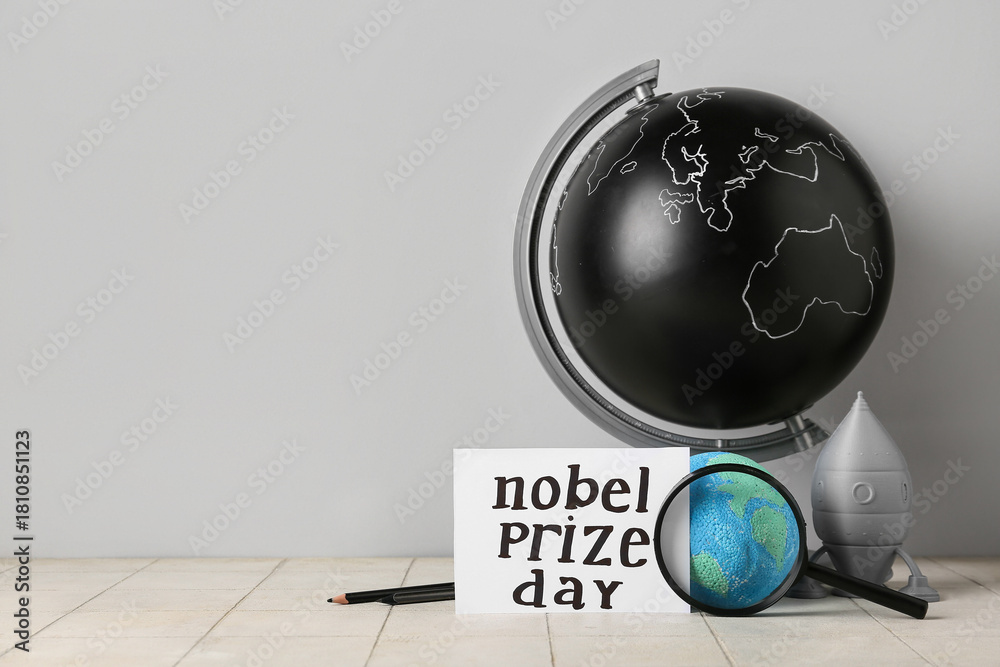 Fototapeta premium Paper with text NOBEL PRIZE DAY, globe, rocket and magnifier on tile against grey background
