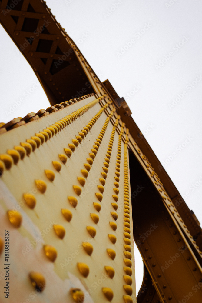 Obraz premium Unique View of Golden Bridge Structure With Detailed Rivets Against a Cloudy Sky
