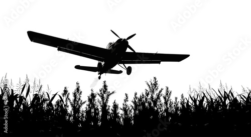 Crop duster airplane flying low over a field of crops in silhouette against a bright sky
