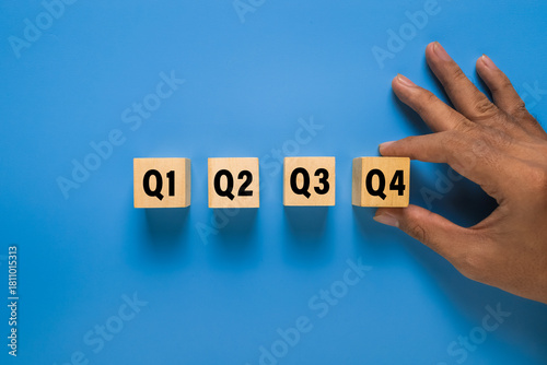 male hand put wooden cubes with q1, q2, q3, q4 symbol isolated on blue background. concept of quarterly report annual