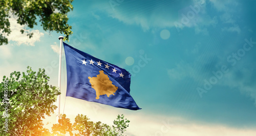 Kosovo national flag waving in the sky behind the tree. The flag blowing with beautiful sunlight. Kosovo national flag for independence day.