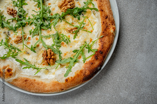 A mouthwatering white pizza sits elegantly on a gray table, showcasing fresh arugula and walnuts