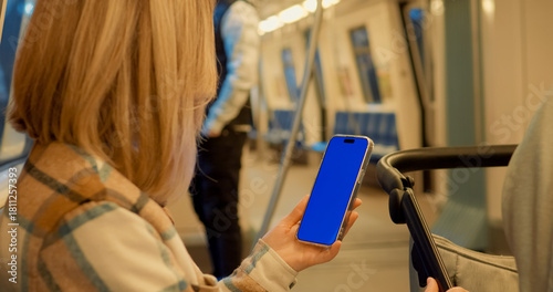 Billede på lærred Urban commuter holding blue screen smartphone while seated inside subway train, showcasing digital communication in modern public transport environment