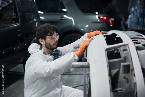 An automotive technician is repairing a car bumper in a workshop while wearing safety gear