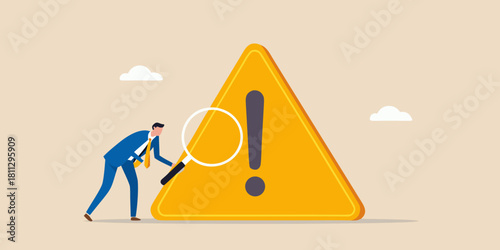 Businessman inspecting a large warning sign with a magnifying glass for risk management