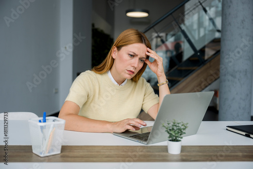Overwhelmed woman with laptop feeling stressed at modern office desk