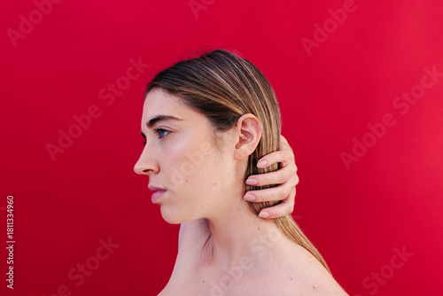 Minimalist side profile portrait with hand on head against red background