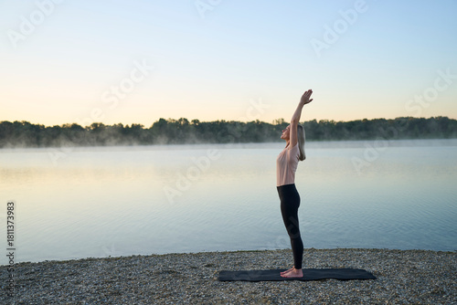 Person practicing yoga at sunrise by a lake in nature outdoors