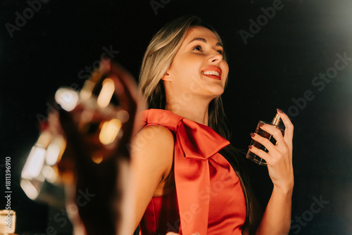 Smiling woman in red dress applies perfume in front of mirror