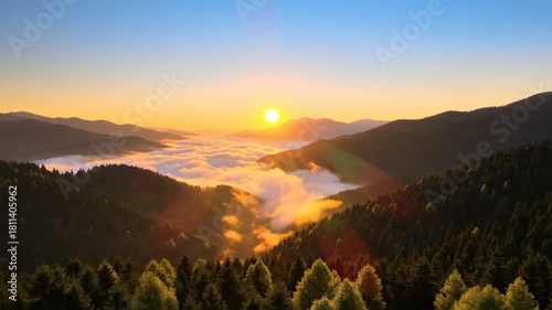 Sunrise over mountain range with low-lying clouds, trees in foreground, bright sun and orange sky