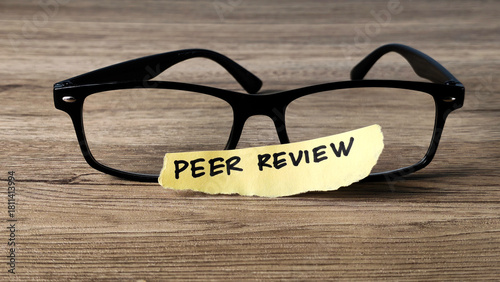 Peer Review concept with a handwritten note placed on reading glasses on a wooden desk, symbolizing academic research and quality assurance.