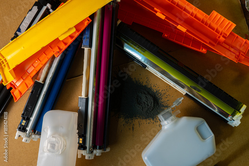 Fotografi Colorful printer cartridges and wasted toner bottles scattered on a cardboard surface with spilled black powder