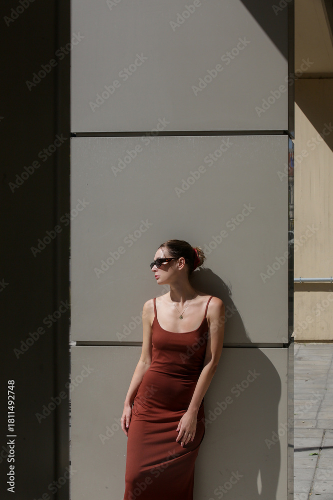 Fototapeta premium Modern young fashionable woman in basic cotton brown camisole dress. Spring summer clothes on a city street. Trendy women's clothing, street fashion trend. 