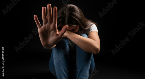 Mujer joven asustada mostrando gesto de pare con la mano y cubriendo su rostro sobre fondo negro. Concepto de violencia de género y miedo.