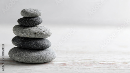 A stack of five smooth, grey and black river stones perfectly balanced on a light wooden surface, symbolizing peace, stability, and harmony.