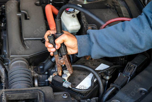 Tableau sur toile A car technician holding a heavy-duty jumper clamp while preparing to jump start a vehicle battery