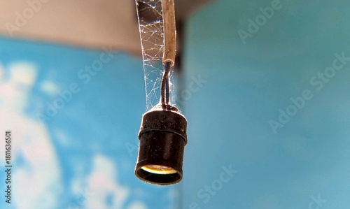 A single hanging light fixture dangles quietly, wrapped in thin cobwebs against faded blue walls. The scene feels abandoned and still, capturing a sense of time passing and the quiet atmosphere of an 