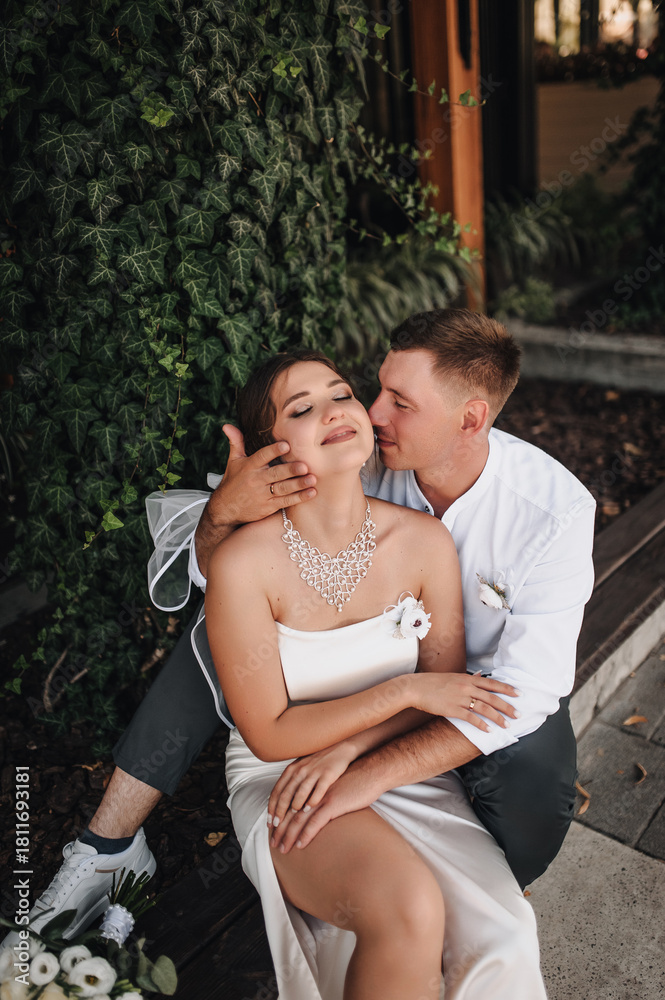 Naklejka premium Wedding photography, portrait of happy smiling newlyweds, fashionable groom and beautiful cute brunette bride, hugging outdoors on the street in the city, in the park.