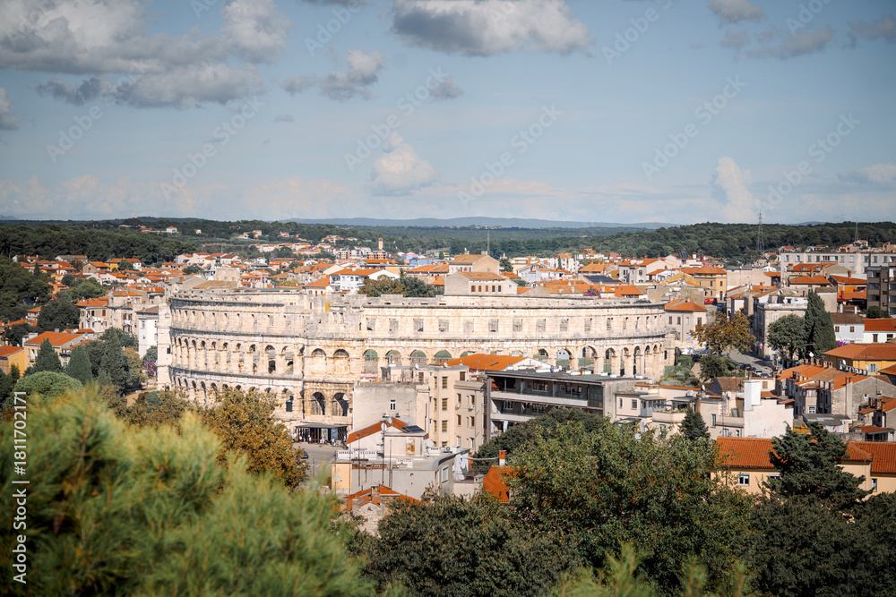 Obraz premium Panoramic cityscape of Pula, Croatia, featuring the ancient Roman amphitheater surrounded by traditional buildings with orange rooftops on a bright summer day.