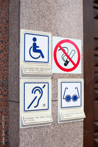 Set of disability icons, including wheelchair, deaf people and blind person. Hearing aid and problems with eyes. Signs at entrance to building for people with disabilities next to no smoking sign