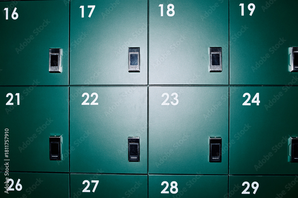 Fototapeta premium Green numbered lockers arranged in grid pattern occupying modern business office wall, metal doors featuring black handles and numbers, providing secure storage for employees