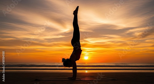 Person practicing handstand yoga pose on a beach at sunset with dramatic sky