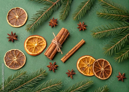 Flat lay featuring cinnamon sticks, dried citrus, christmas tree branches on a green background