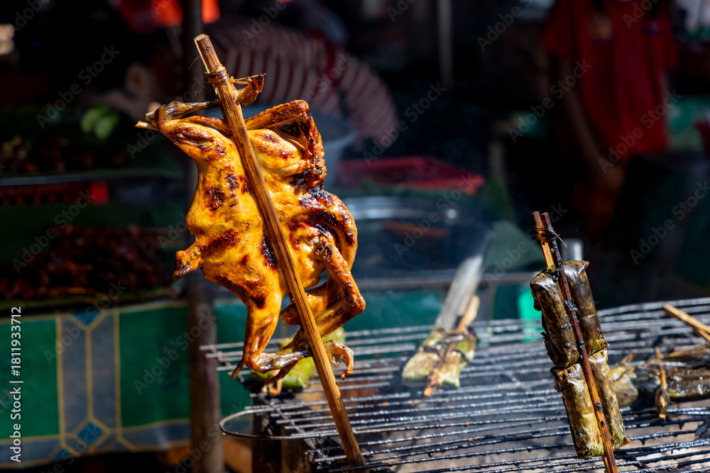 Fototapeta premium Grilled chicken browning on a bamboo skewer above a charcoal grill at a local street food stall in siem reap, cambodia