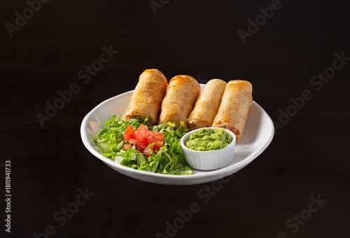 Chicken flauta platter with a fresh garden salad and guacamole in a white plate on a dark surface, appetizer, 